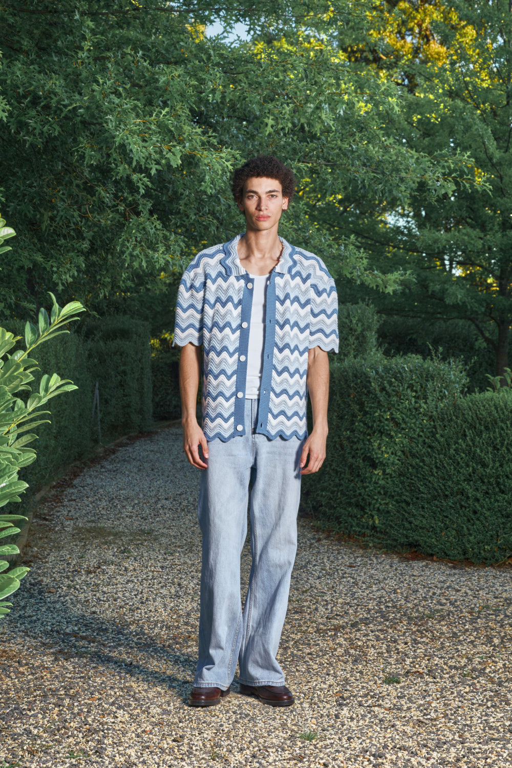 Full view for a model wearing a blue and white shale stitch knit shirt over a white top, standing outdoors.