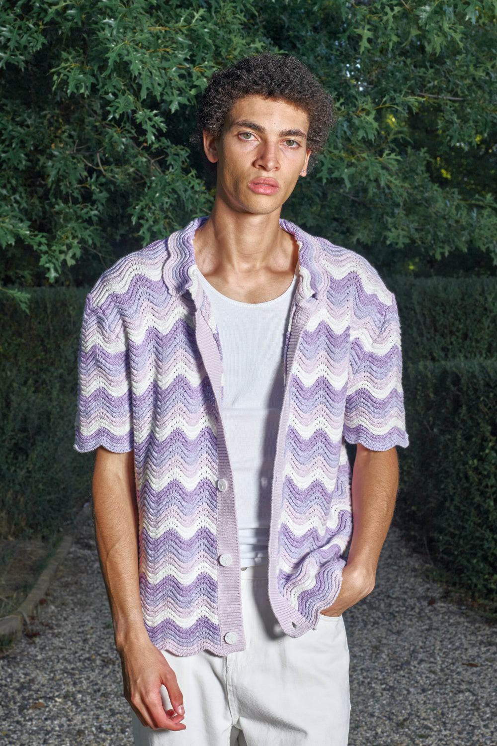 Man wearing a purple and white patterned shirt outdoors with greenery in the background