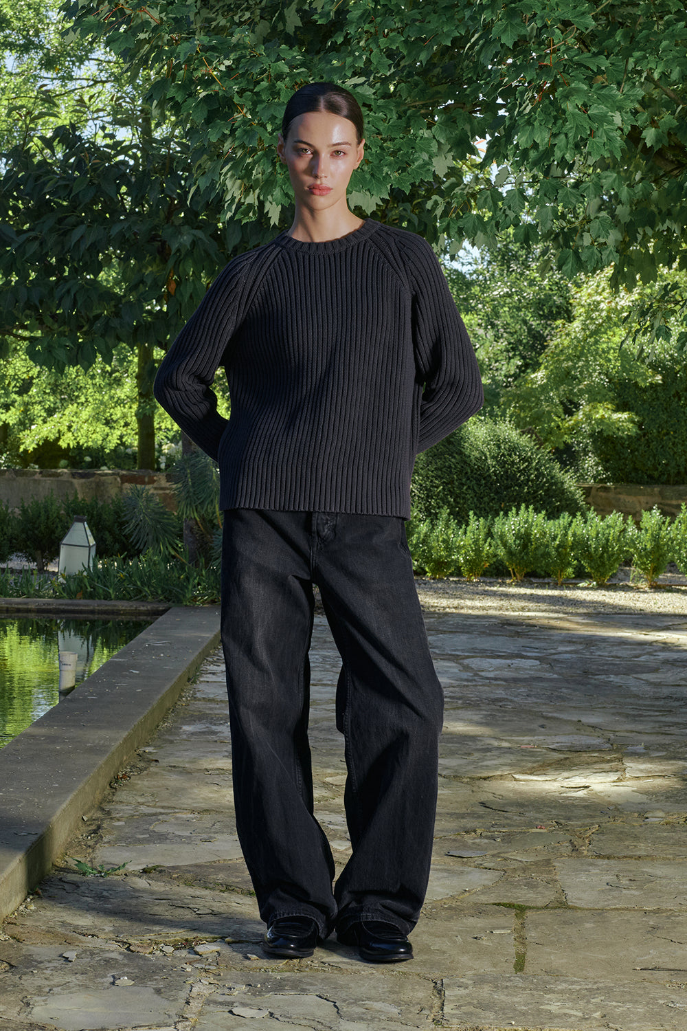 Model wearing a black ribbed knit sweater with black pants.