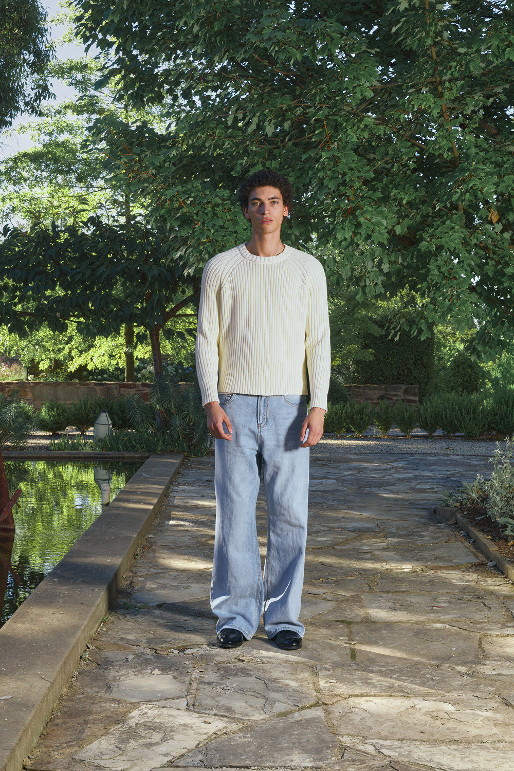 Model wearing a cream ribbed knit sweater with light jeans, standing outdoors.