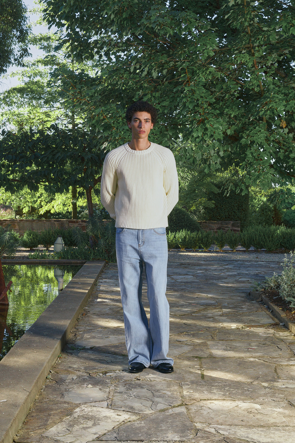 Model wearing a cream ribbed knit sweater with light jeans, standing outdoors.