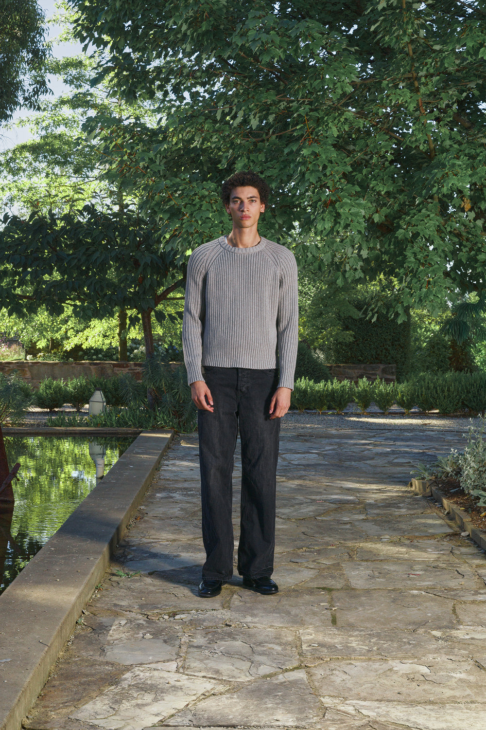 Model wearing a grey ribbed knit sweater with a black jeans, standing outdoors.
