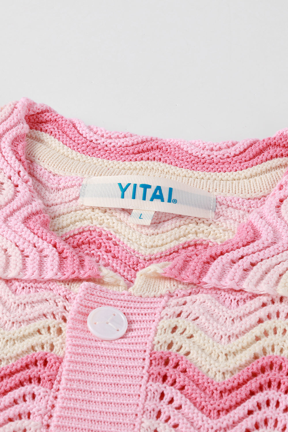 Close-up of pink and cream shell stitch crochet shirt with scalloped collar, white button closure, and YITAI label.