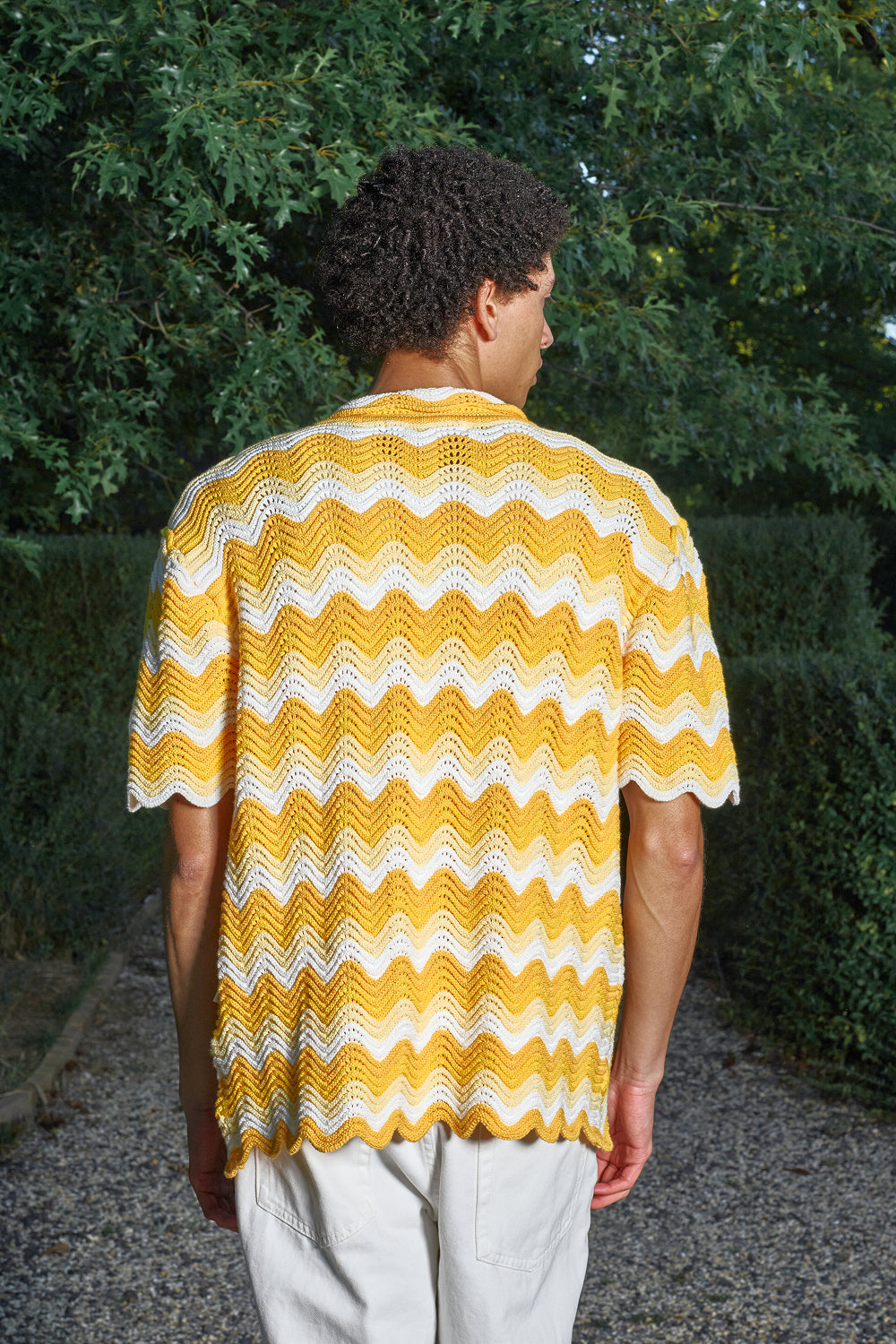 Back view of a model wearing a yellow and white shale stitch knit shirt.