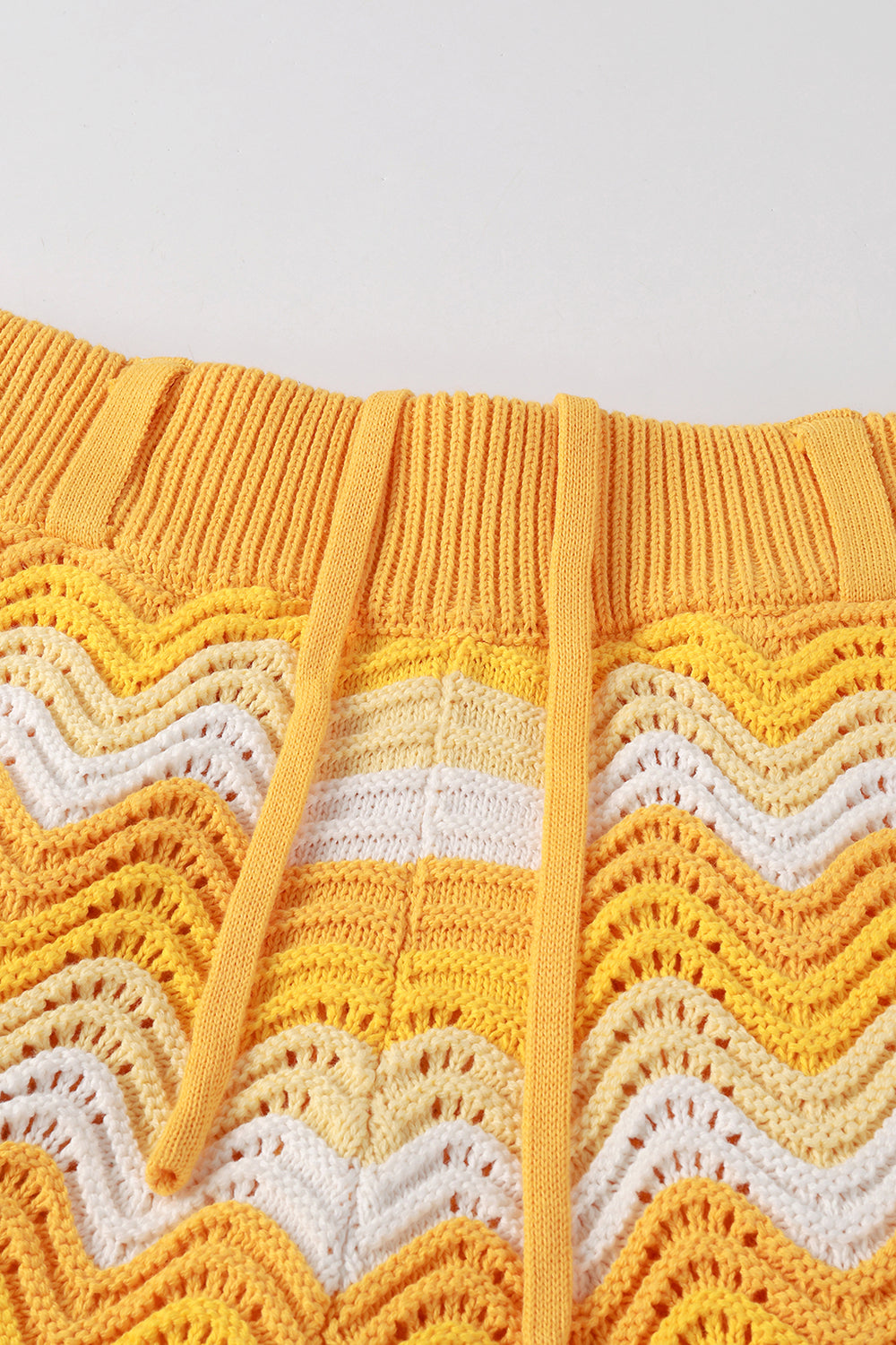 Close-up of yellow and white shale stitch knit shorts with drawstring waistband.