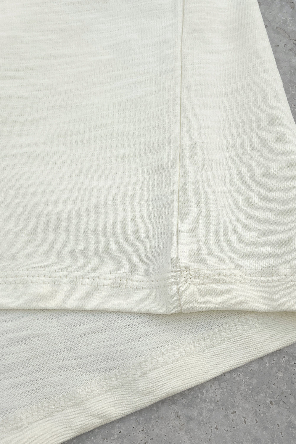 Close-up of the bottom hem and side seam of a cream T-shirt showing stitching and fabric texture details.