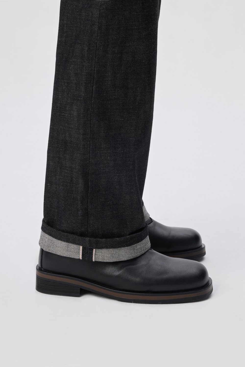 Close-up of the cuffed hem of black denim trousers, showing the contrasting selvedge edge.