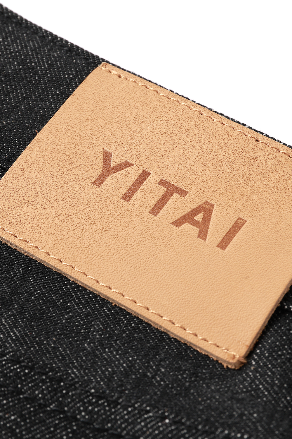 Close-up of the tan YITAI leather waistband patch on black denim.