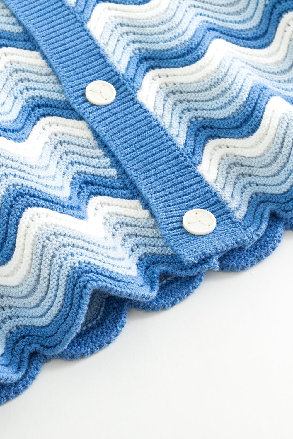 Close-up of the hem and front placket of a blue and white shale stitch knit shirt, showing the scalloped hem and front buttons.