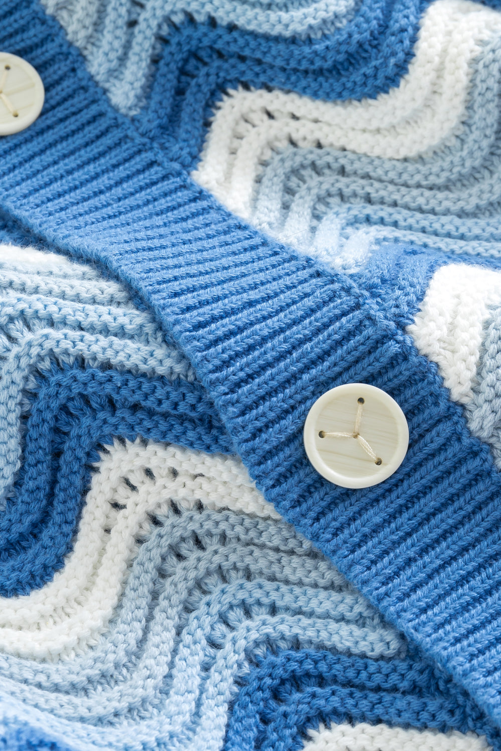 Close-up of the front placket of a blue and white shale stitch knit shirt with buttons.