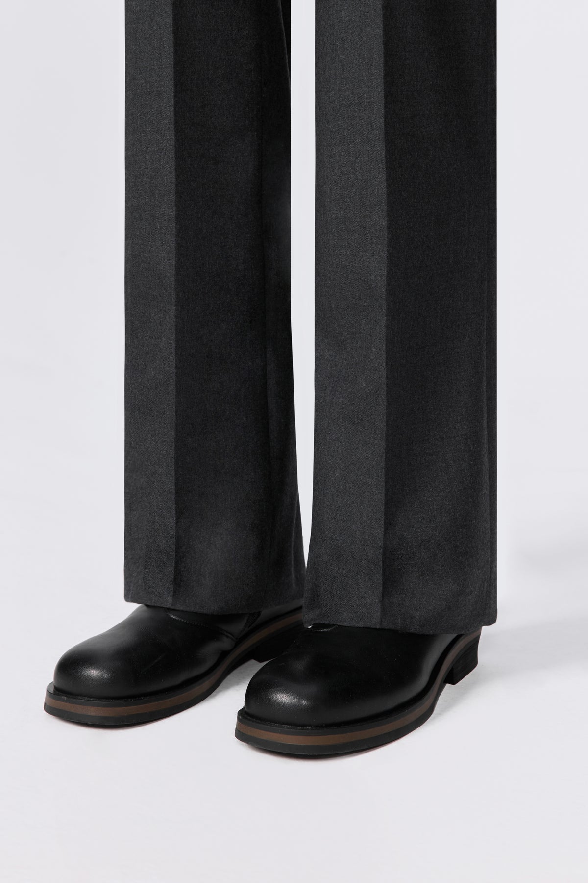 Close-up of charcoal wool trousers hem and cuff with black leather boots.