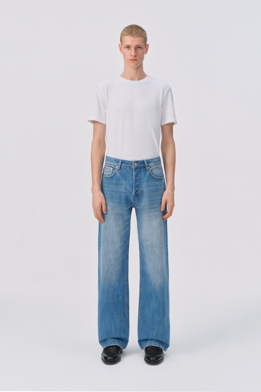 Full-length front view of a man in a white t-shirt and light-wash straight-leg jeans.
