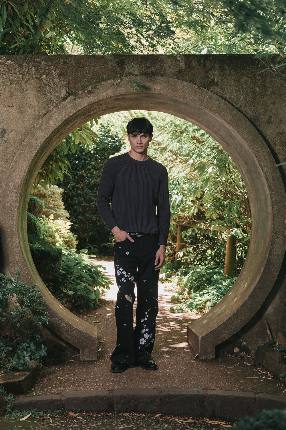 Model wearing black denim pants with floral embroidery, full-length view.
