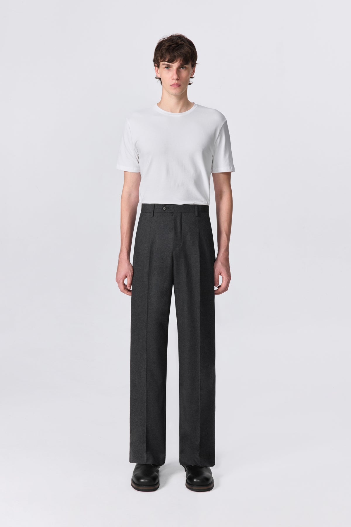 Cropped front view of model wearing charcoal relaxed straight-leg fit wool trousers with white t-shirt and black boots.