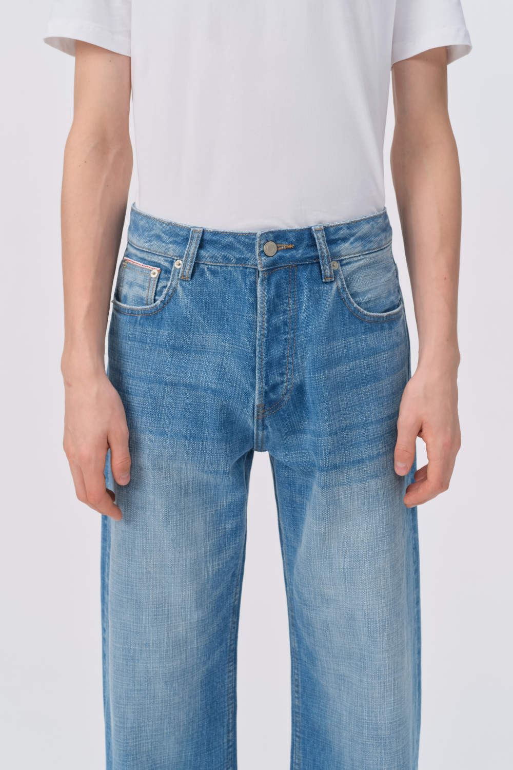 Close-up of light-wash wide-leg jeans on a model, showing the button fly, front pockets, and faded whisker detailing at the hips.