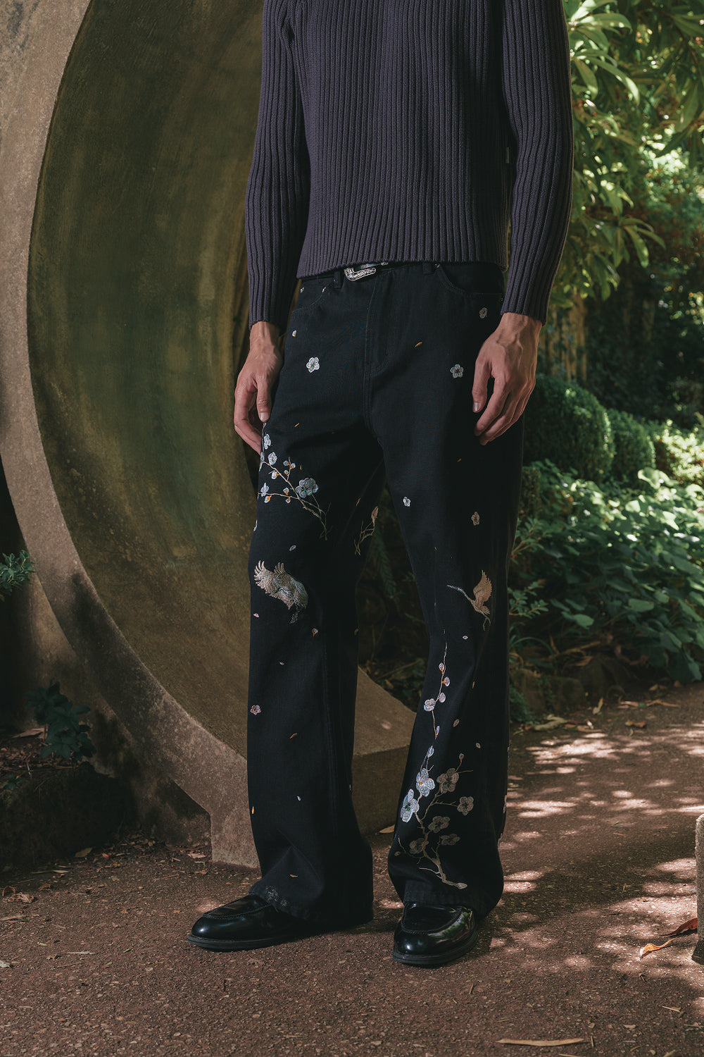 Model wearing black embroidered denim pants, front embroidery detail