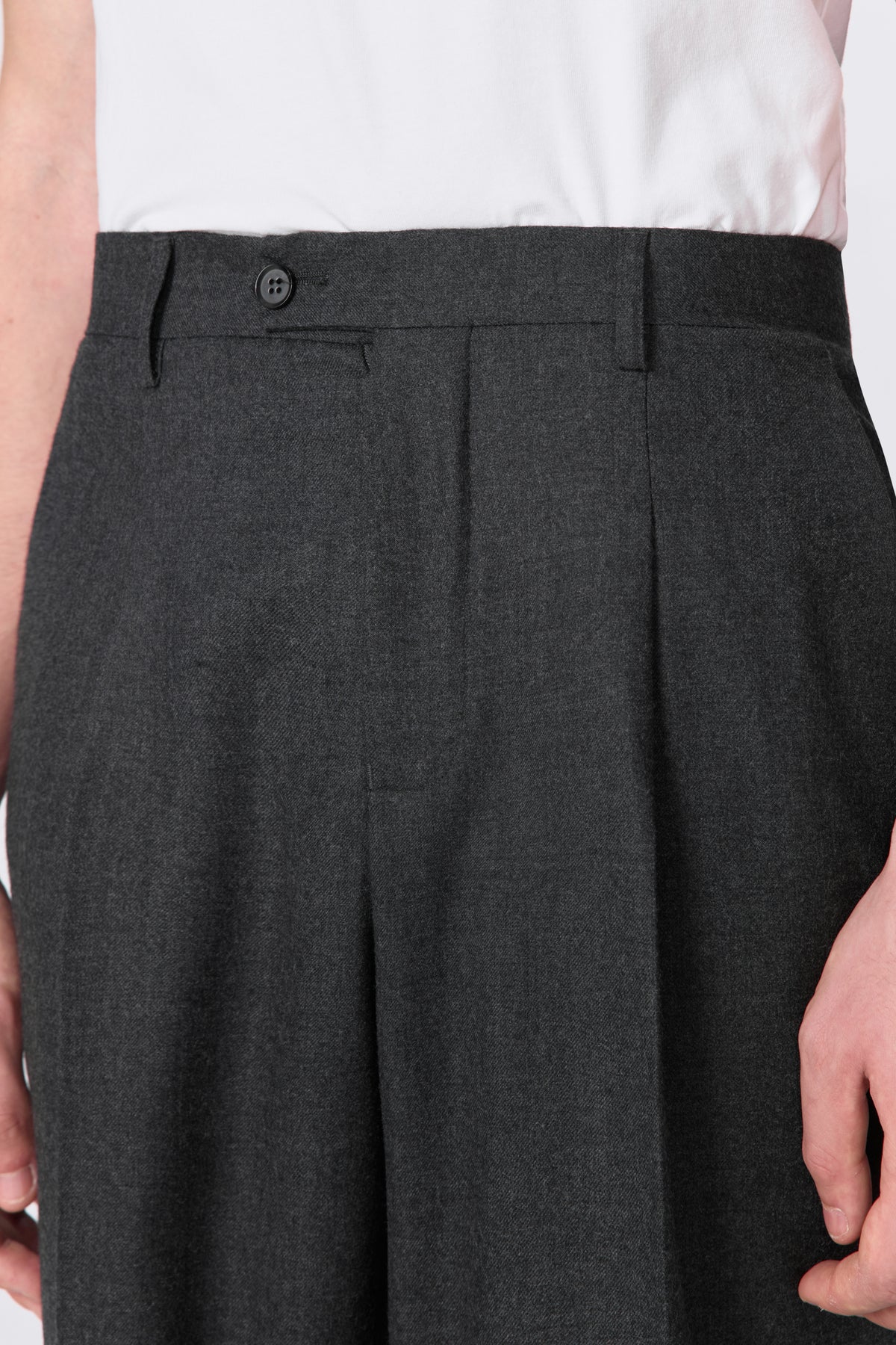 Close-up of charcoal wool trouser waistband showing button closure and front pleat