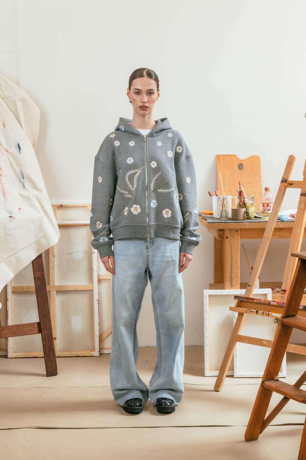 Full view of a model wearing a grey hoodie with floral embroidery, paired with light blue denim.