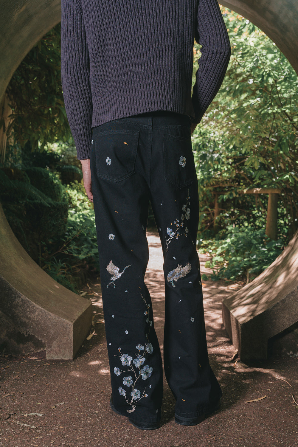 Back view of model wearing black chinoiserie embroidered denim pants