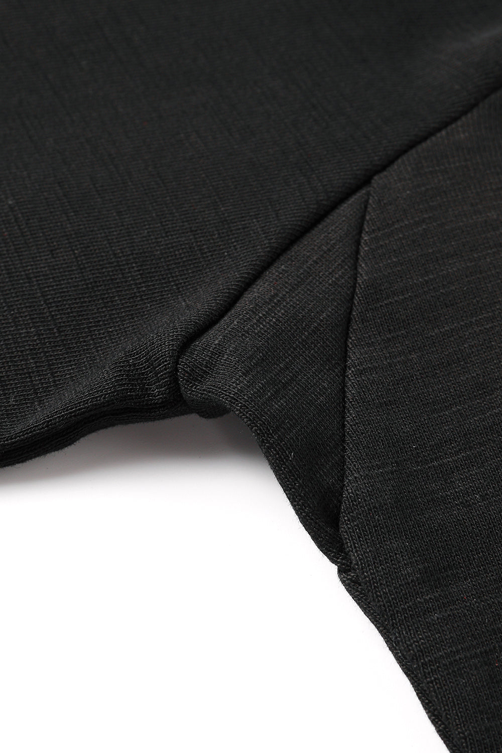 Close-up of the sleeve and side seam of a Black T-shirt laid flat on a gray textured surface, highlighting the soft fabric and stitching details.