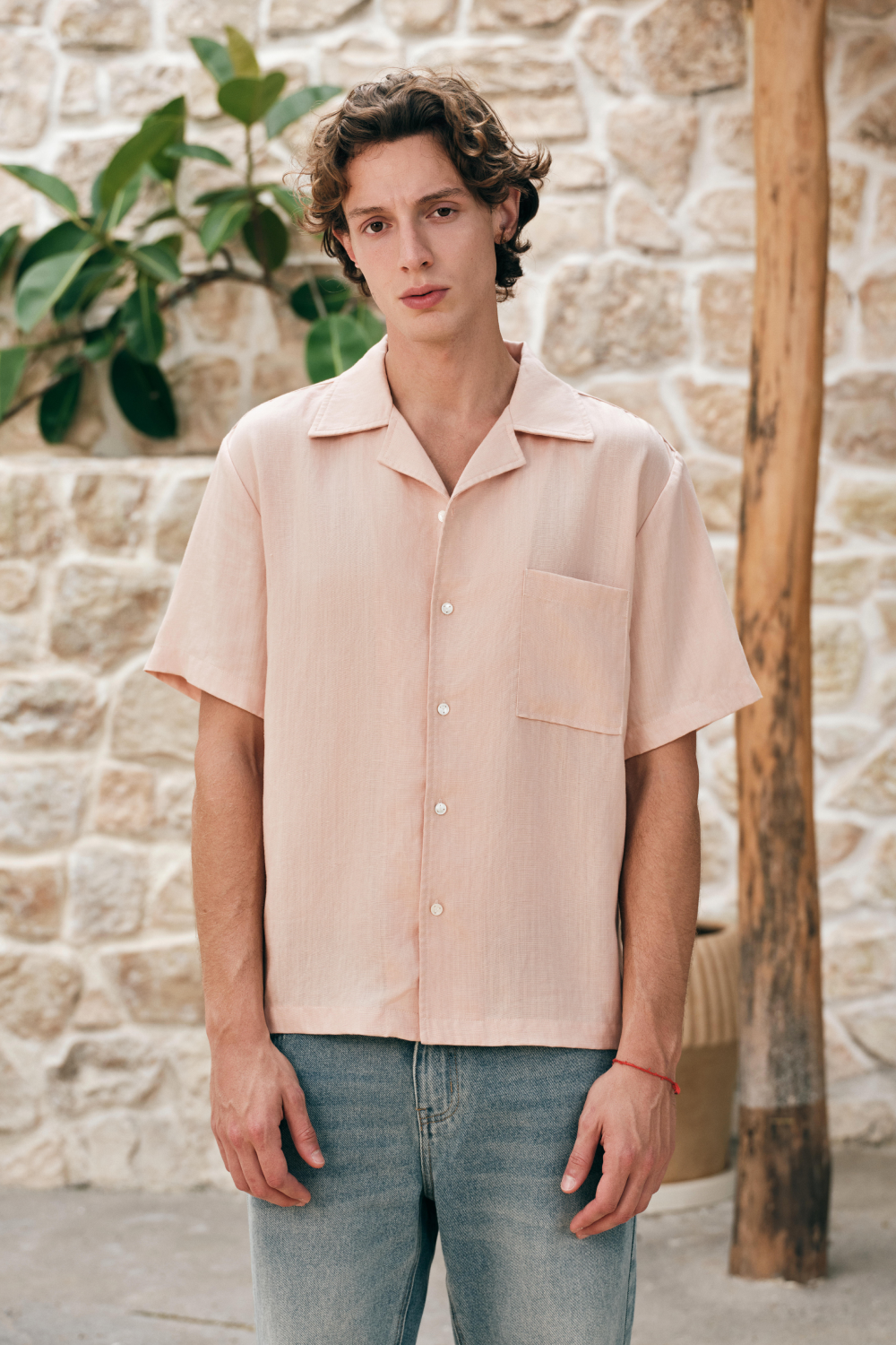 Model wearing a light pink short-sleeve button-front shirt with a camp collar and chest patch pocket.