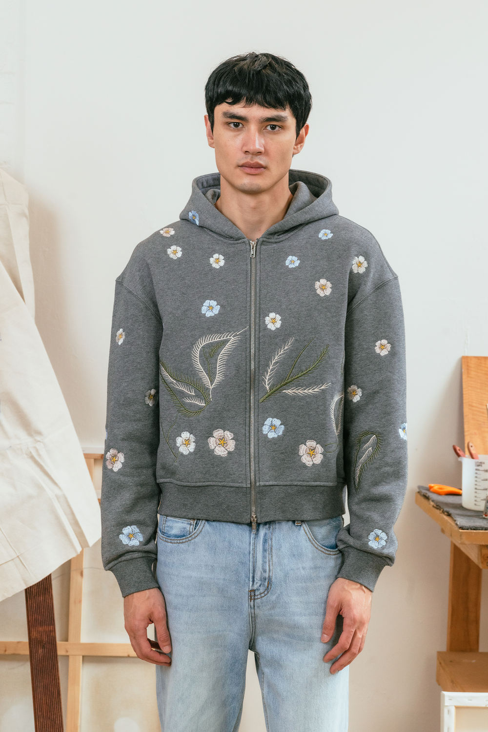 Person wearing a grey hoodie with floral embroidery in a casual setting