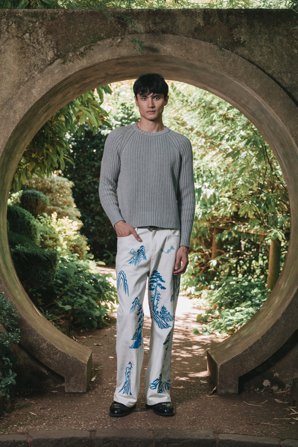 Full-length view of model wearing white denim pants with blue embroidery.