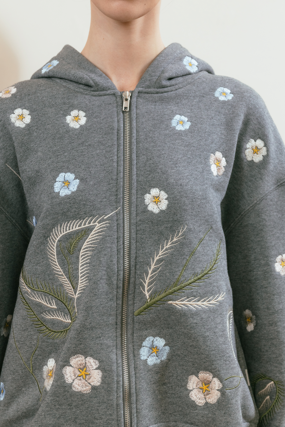 Grey hoodie with floral and leaf embroidery on a neutral background
