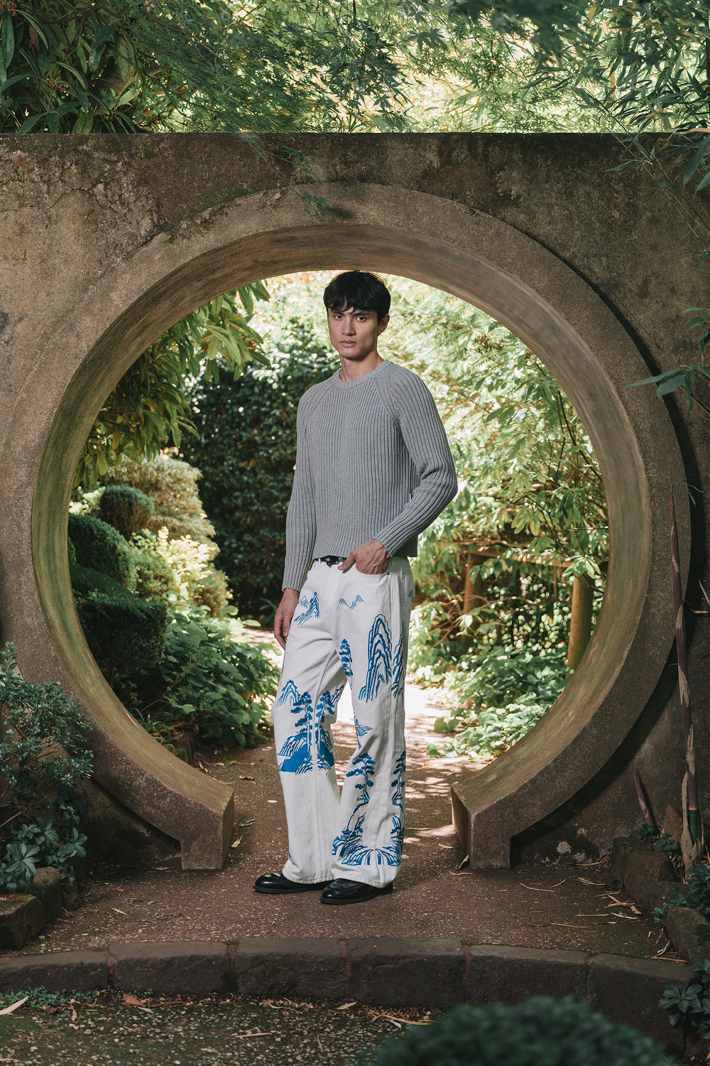 Full-length front view of model wearing white denim pants with blue embroidery.