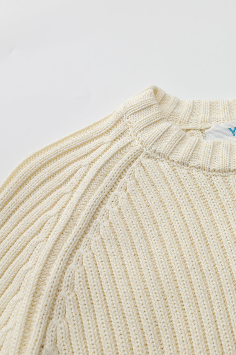 Close-up of a ribbed knit sweater collar with a brand tag on white background