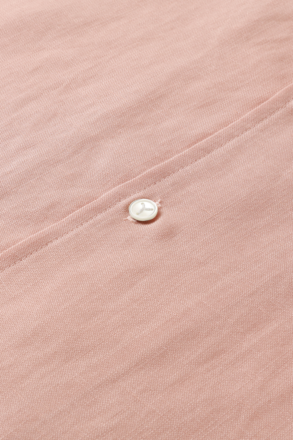 Close-up of light pink shirt with front button placket and mother-of-pearl button.