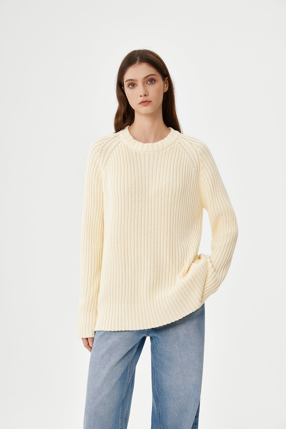 Woman wearing a cream ribbed sweater and blue jeans on a white background