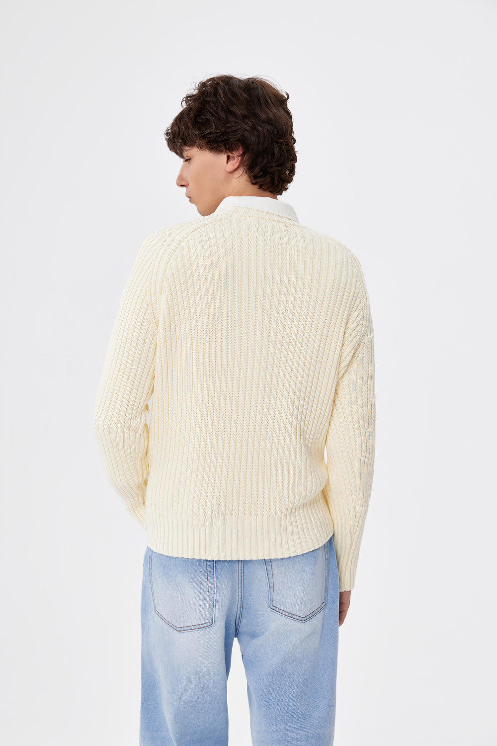 Person wearing a cream ribbed sweater and light blue jeans on a white background