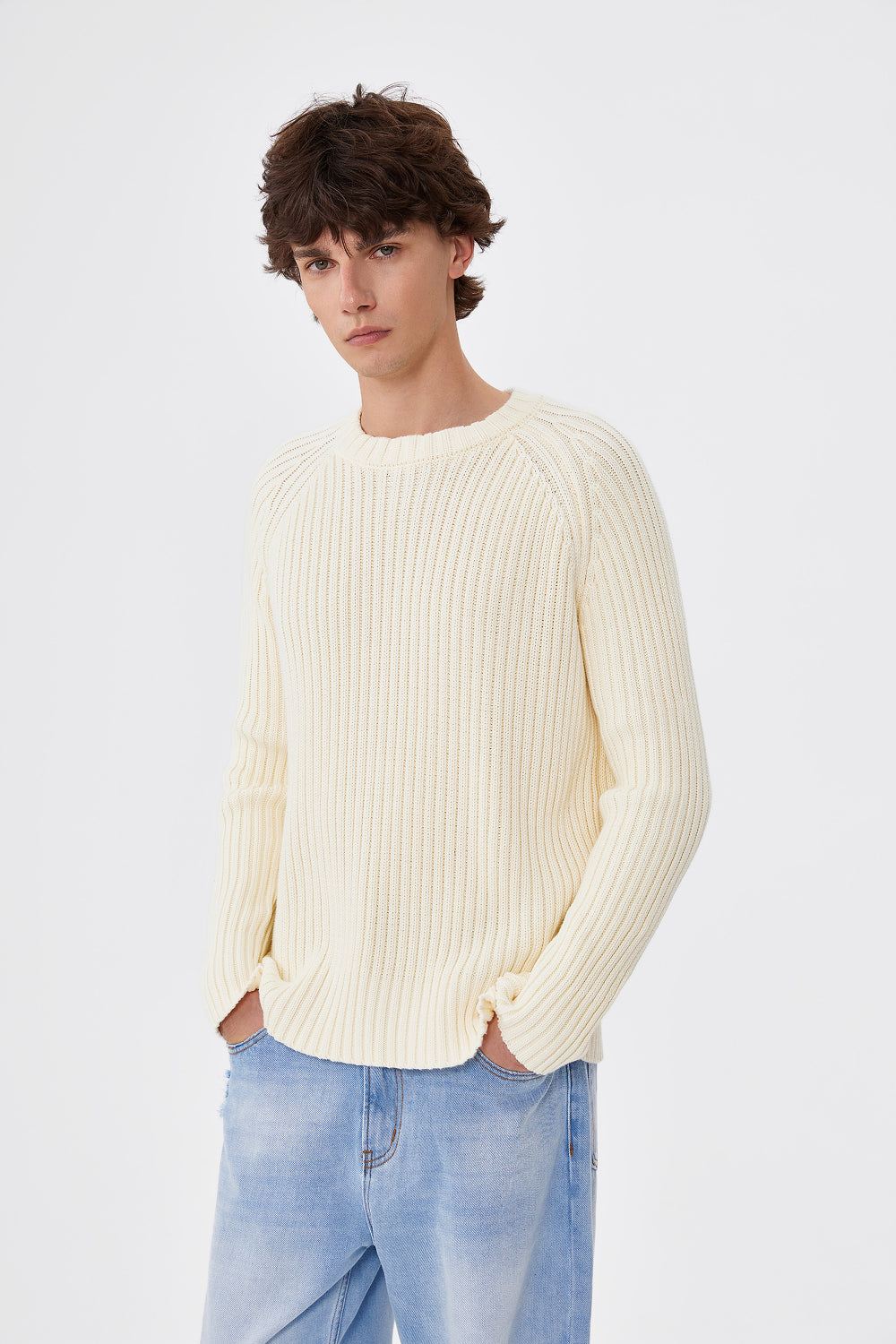 Person wearing a cream ribbed sweater and light blue jeans on a white background