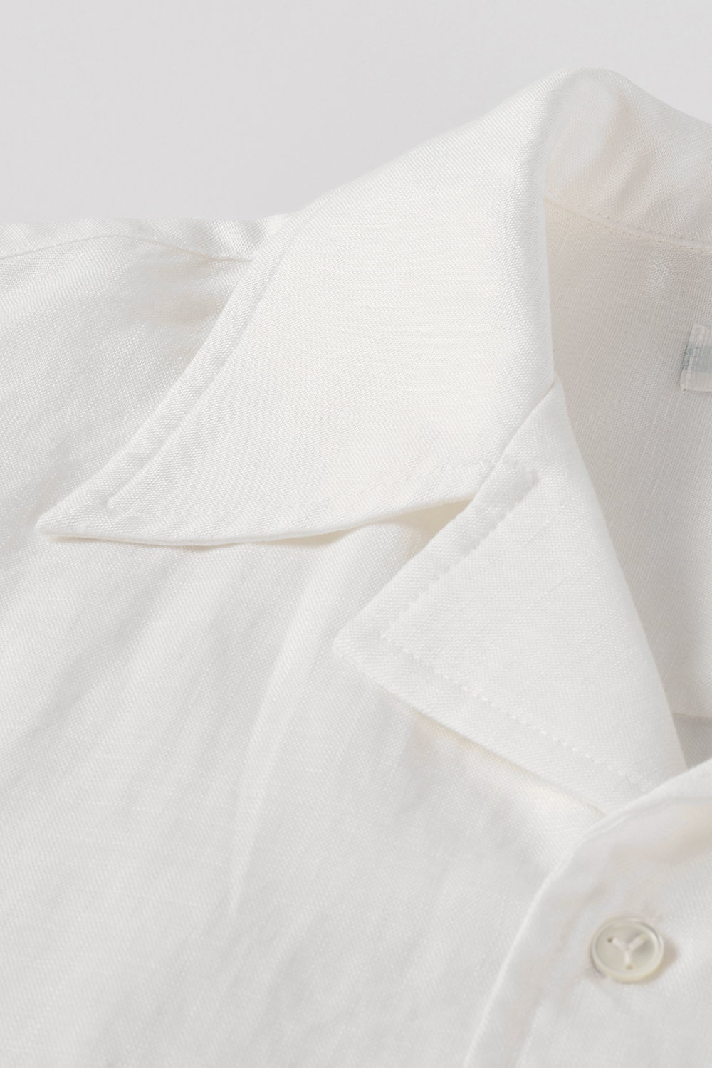 Close-up of white shirt with a camp collar and mother-of-pearl button.