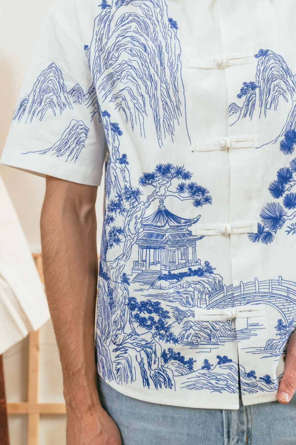 Close-up view of a white shirt with blue traditional embroidery and Chinese knot buttons.