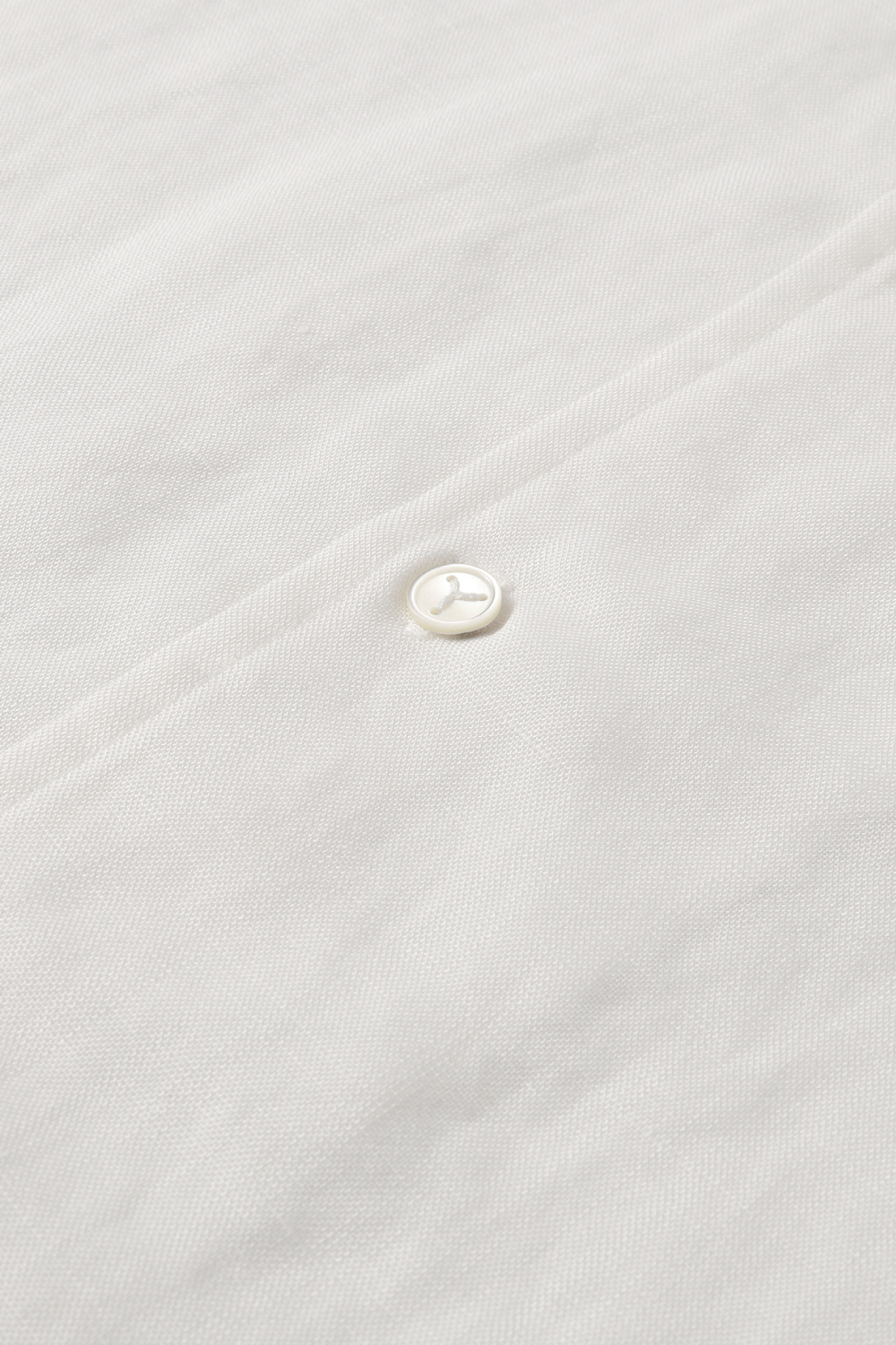 Close-up of a white shirt with front button placket and mother-of-pearl button.