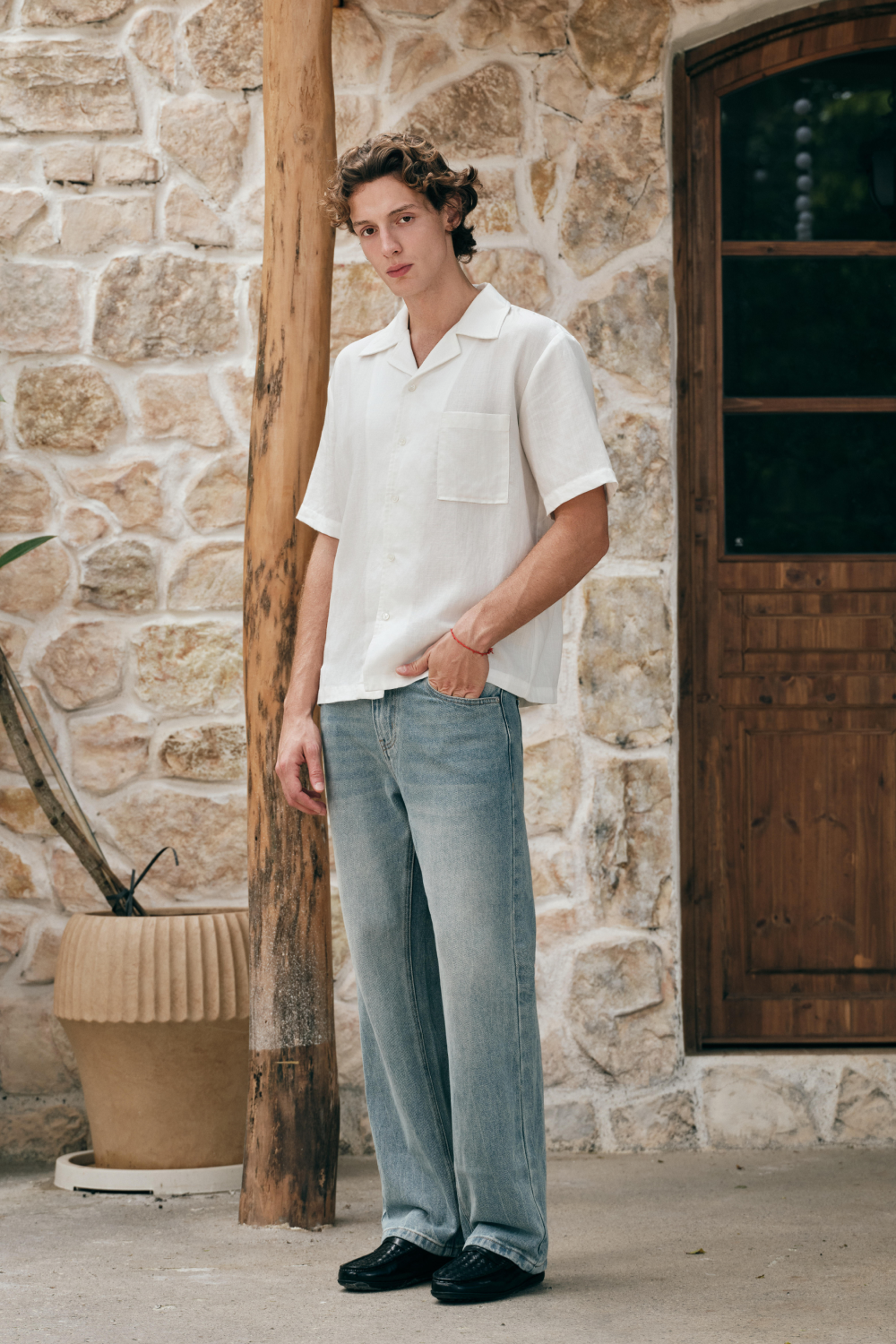Full length view of a model wearing a white short-sleeve button-up shirt with an open collar and chest patch pocket, styled with a light blue jeans.