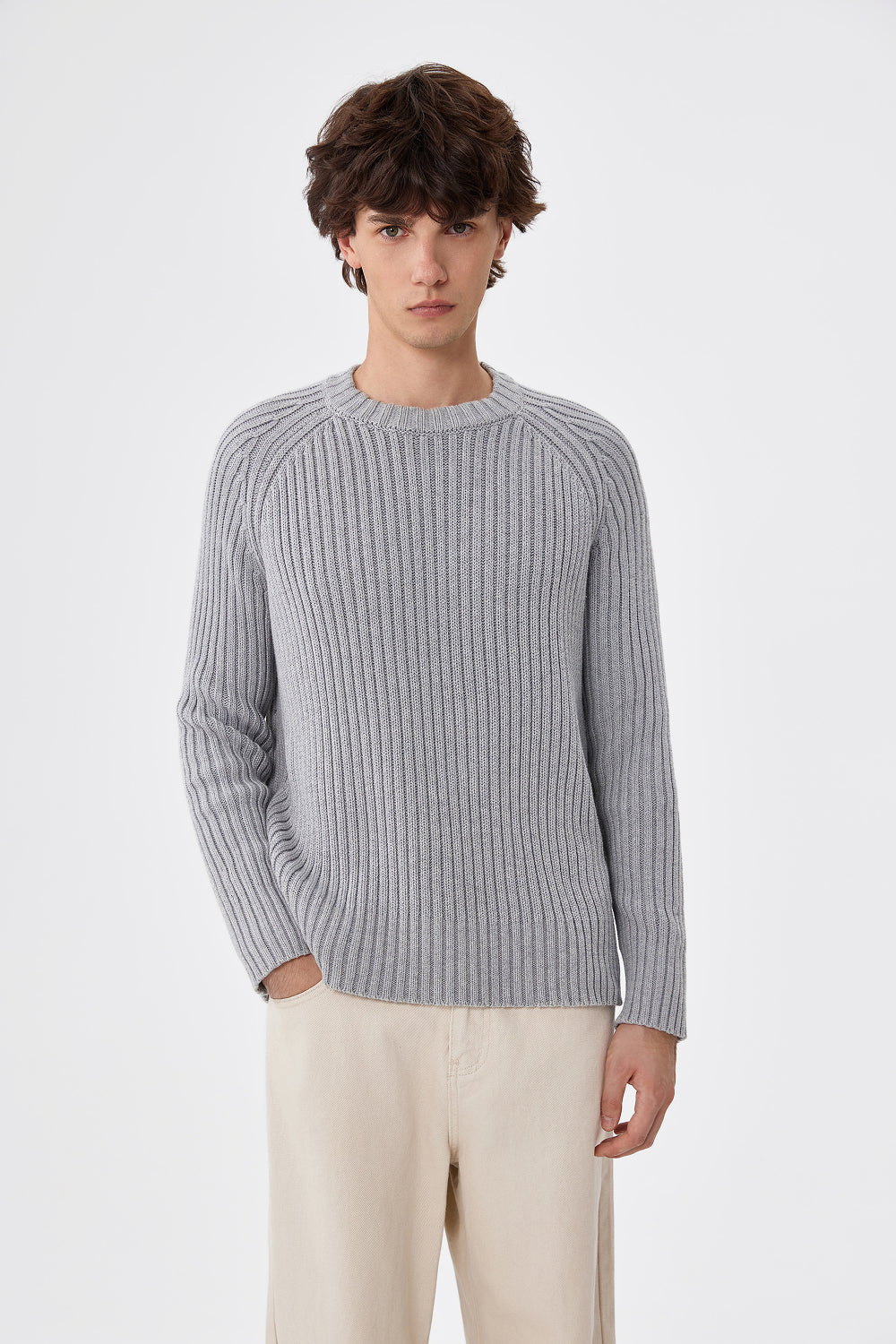 Person wearing a gray ribbed sweater and beige pants on a white background