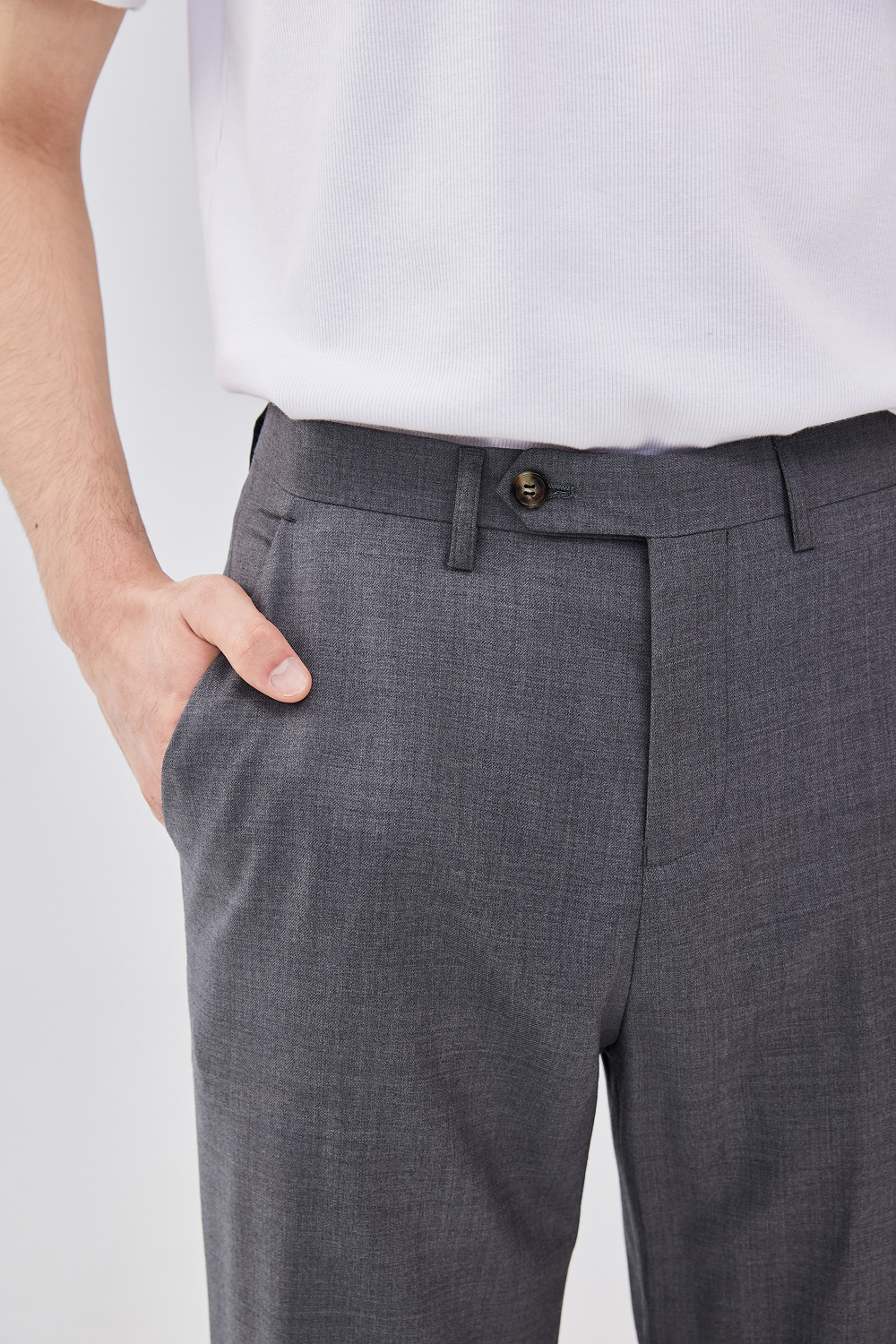Close-up of a model wearing straight-leg grey wool trousers, showing the front waistband, button closure, belt loops, and side pocket.