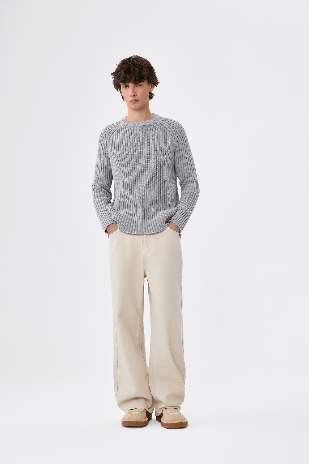 Person wearing a gray ribbed sweater and beige pants on a white background