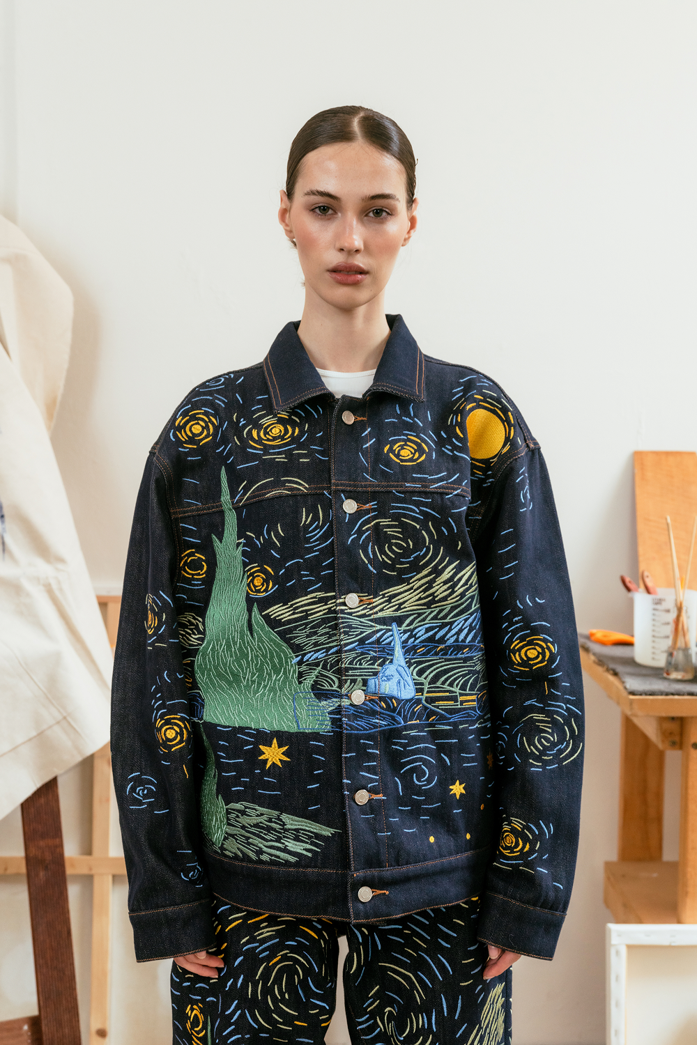 Model wearing a dark denim jacket with Starry Night-inspired embroidery paired with matching embroidered denim jeans.