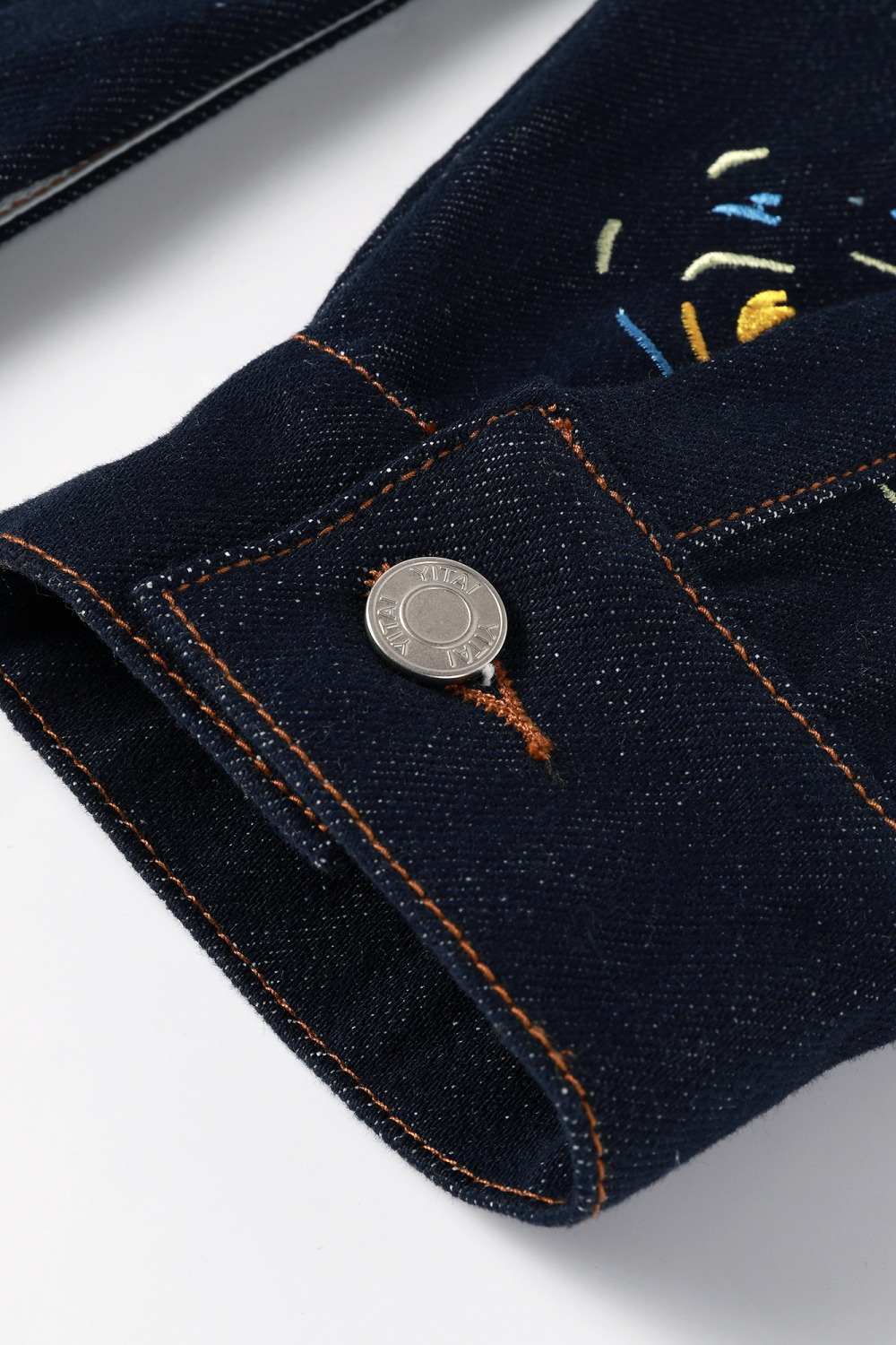 Close-up of dark denim cuff with contrast stitching and a silver metal button.