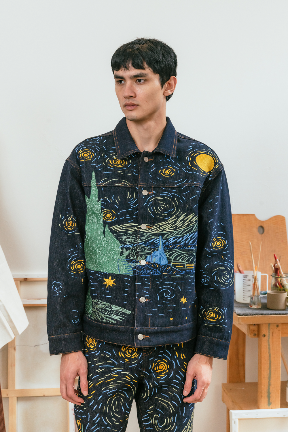 Person wearing a dark denim jacket with Starry Night-inspired embroidery in blue, yellow, and cream, paired with matching embroidered denim jeans.