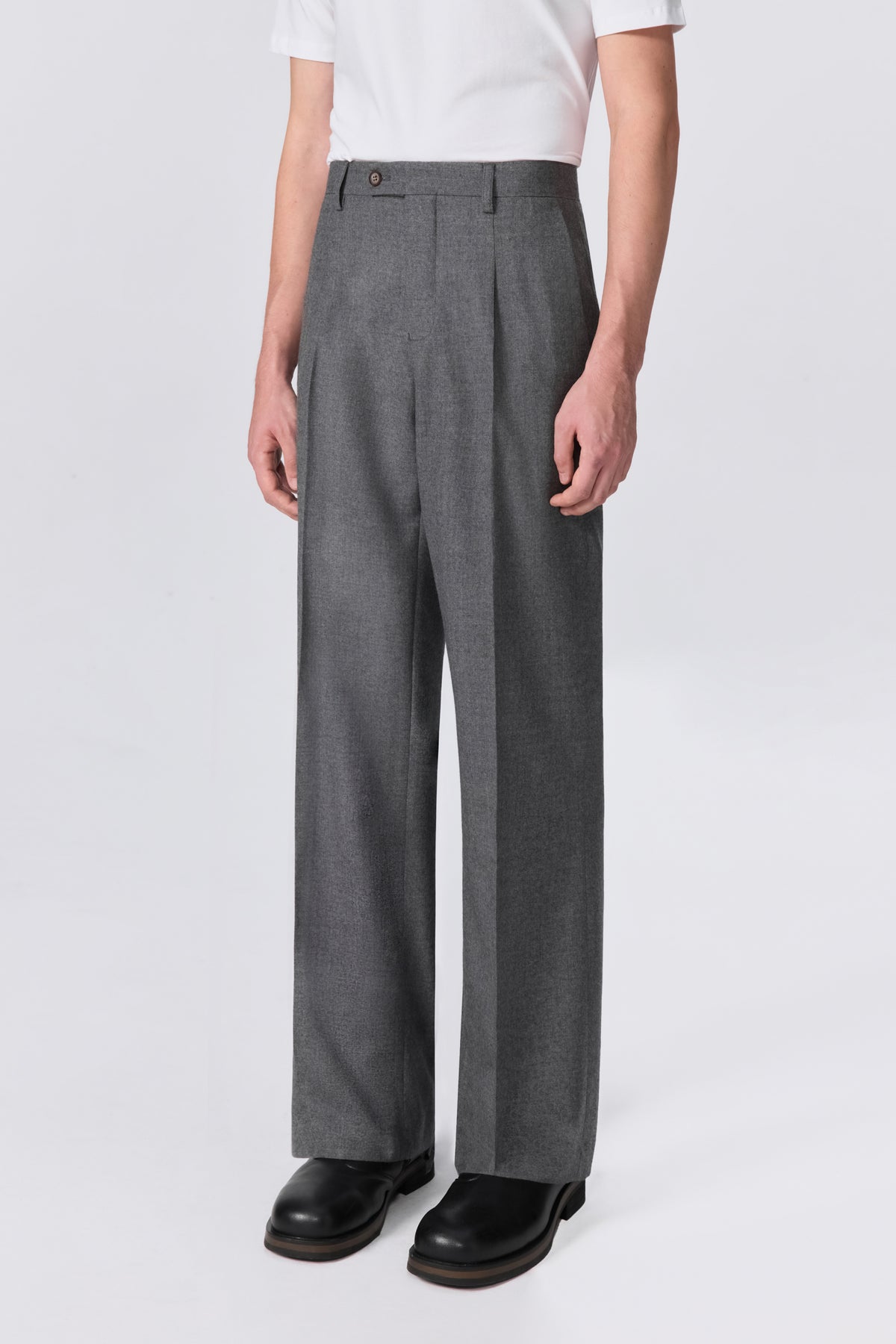 Side angle view of model wearing grey pleated wool trousers showing relaxed straight-leg fit silhouette