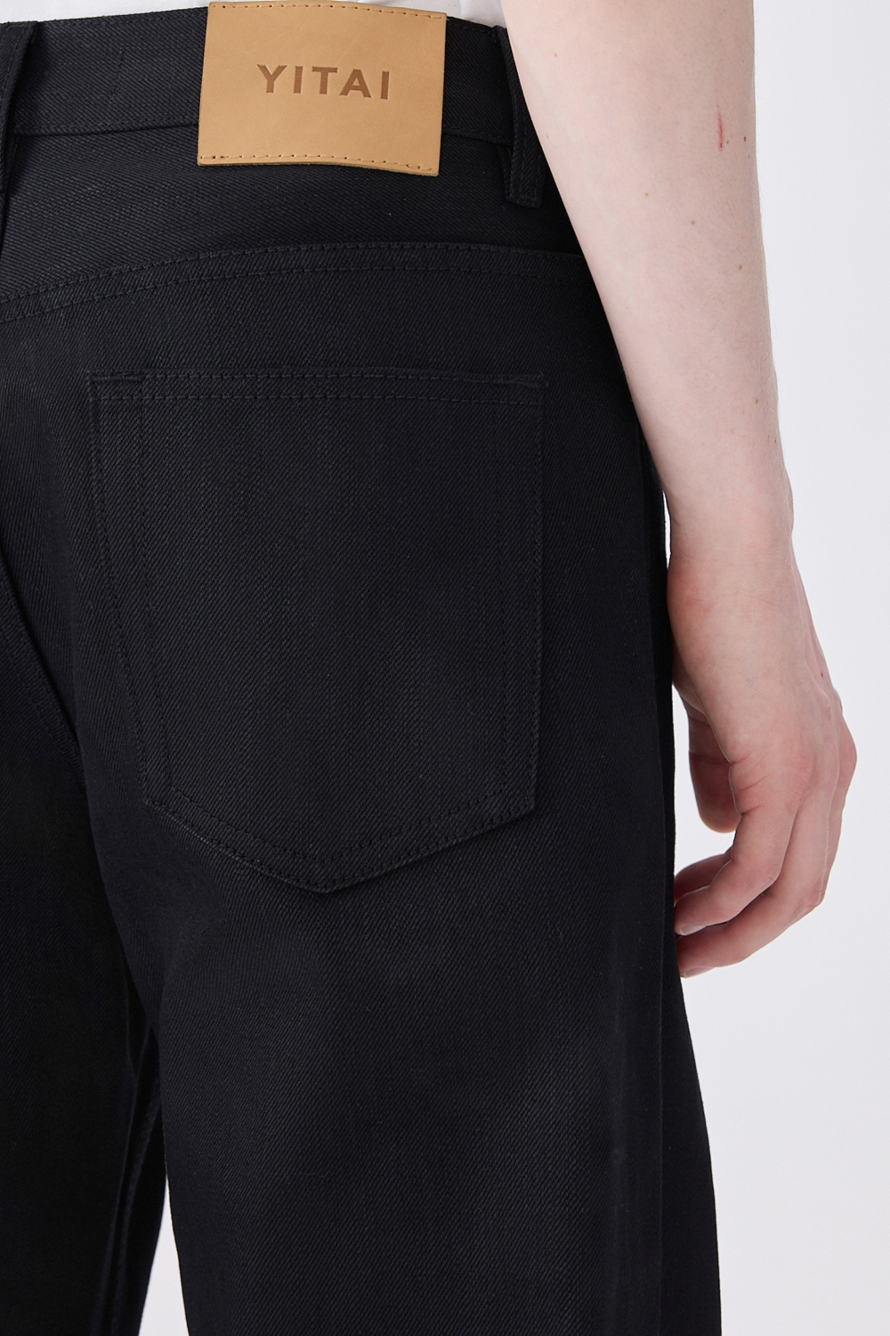Close-up of black selvedge denim jeans showing the back pocket and YITAI leather waistband patch.
