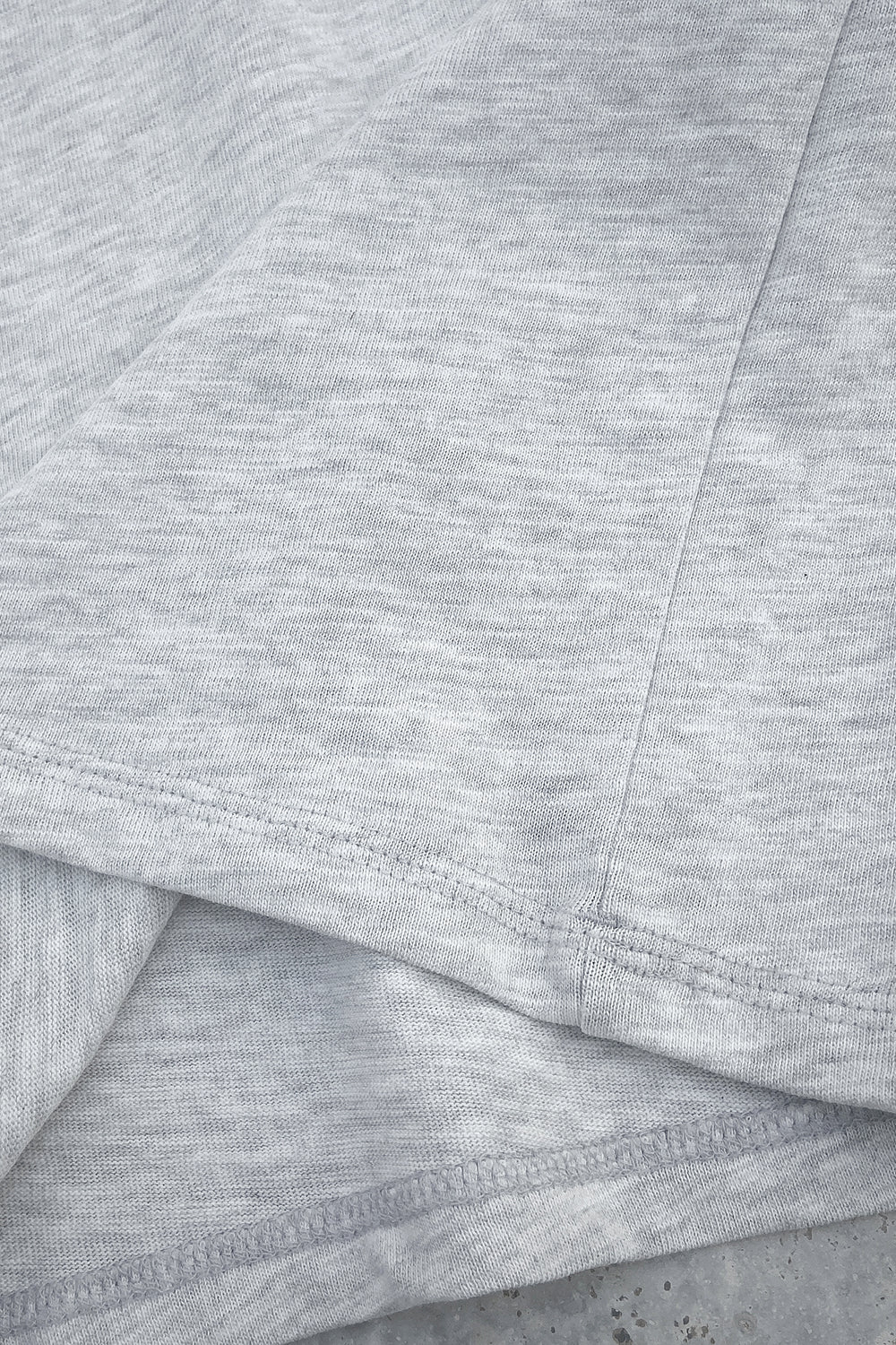 Close-up of the bottom hem and side seam of a grey T-shirt showing stitching and fabric texture details.