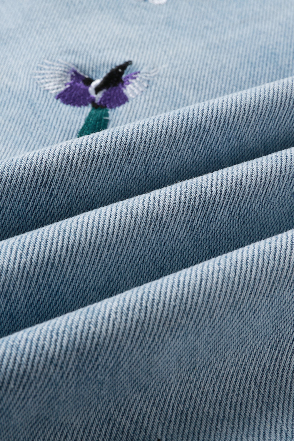 Close-up of blue denim fabric with embroidered bird design