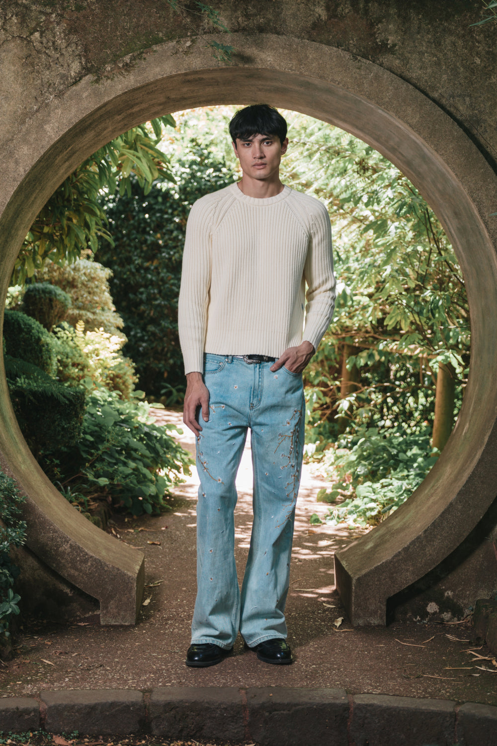 Model wearing light blue denim jeans with bird and branch embroidery, full-length front view outdoors.