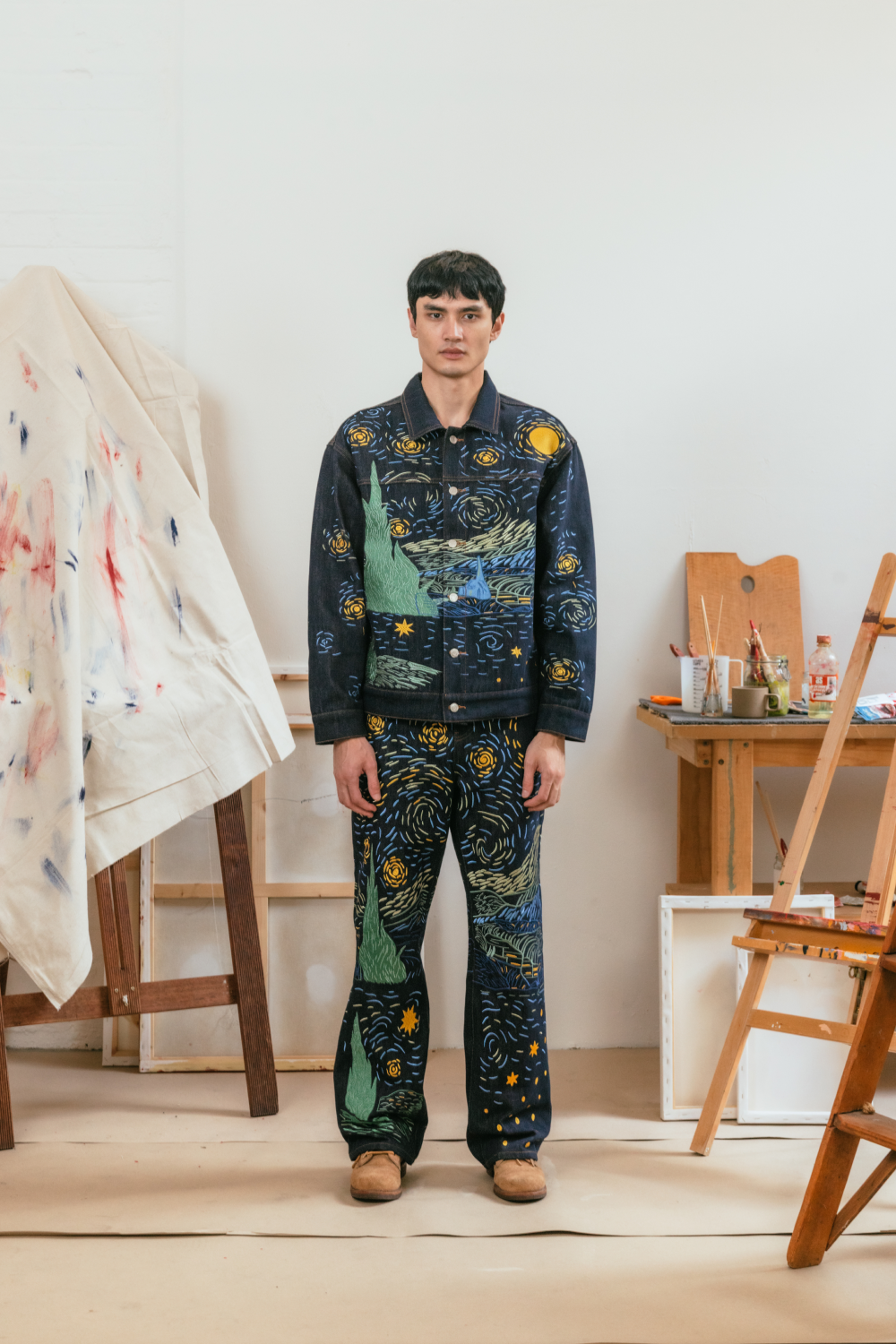 Model wearing a matching Starry Night-inspired denim jacket and jeans set with blue and yellow embroidery.